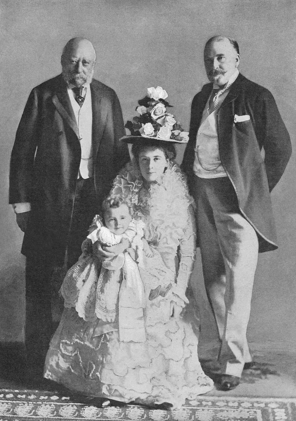 Four generations of one family in a studio portrait from 1900, a great-grandfather and his son standing behind a seated young mother holding her baby